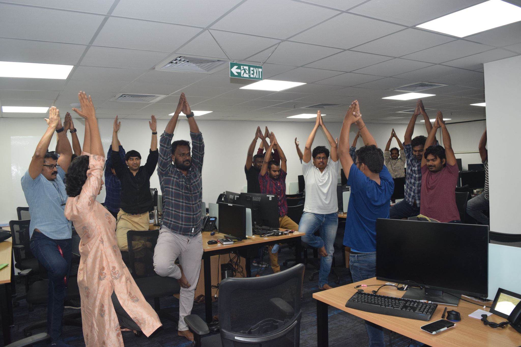 Employees practicing Vrikshasana (Tree Pose) during a Yoganta corporate yoga and workplace wellness session.